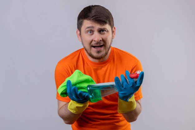 Jeune homme portant un t-shirt orange et des gants en caoutchouc tenant un spray de nettoyage et un tapis à l'irritation