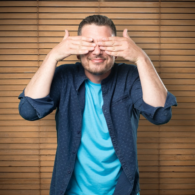 Jeune homme portant une tenue bleue. Sourire et couvrant ses yeux w