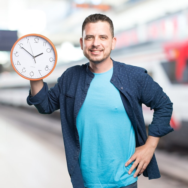 Photo gratuite jeune homme portant une tenue bleue. la tenue d'une horloge. souriant.