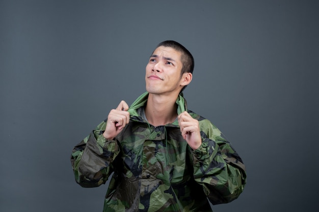 Le jeune homme porte un imperméable de camouflage et montre différents gestes.