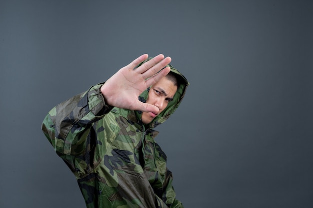 Le jeune homme porte un imperméable de camouflage et montre différents gestes.