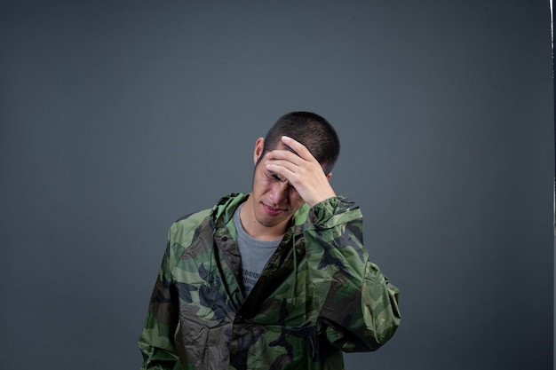 Le jeune homme porte un imperméable de camouflage et montre différents gestes.