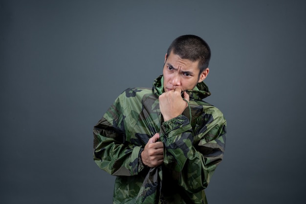 Le jeune homme porte un imperméable de camouflage et montre différents gestes.