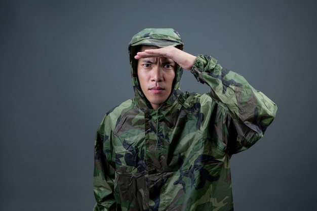 Le jeune homme porte un imperméable de camouflage et montre différents gestes.