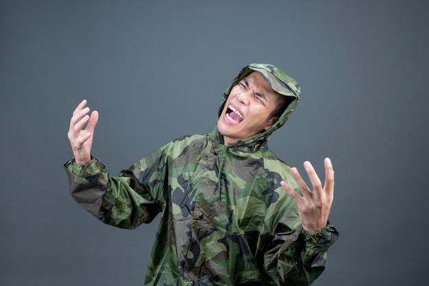 Le jeune homme porte un imperméable de camouflage et montre différents gestes.