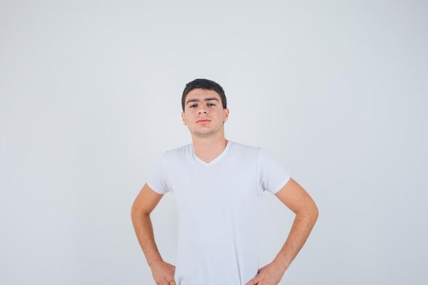 Photo gratuite jeune homme posant avec les mains sur la taille en t-shirt et à la confiance en soi, vue de face.