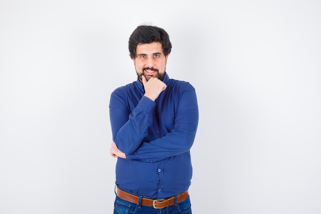 Jeune homme posant en souriant en chemise bleu royal et l'air heureux, vue de face.