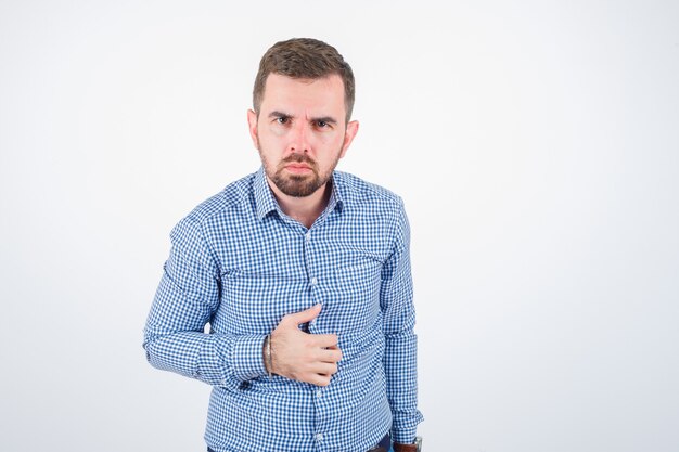 Jeune homme posant tout en regardant la caméra en chemise et à la vue sérieuse, de face.