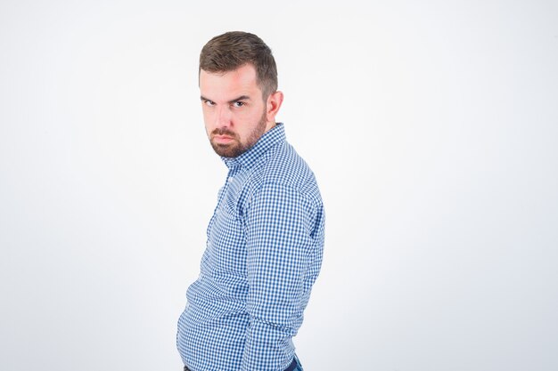 Jeune homme posant tout en regardant la caméra en chemise et à la vue sérieuse, de face.