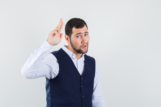 Jeune homme posant tout en tenant deux doigts ensemble en chemise, gilet et à la confiance