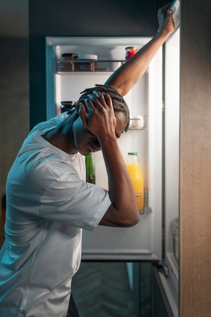 Photo gratuite jeune homme prenant une collation au milieu de la nuit à la maison à côté du réfrigérateur