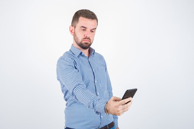 Jeune homme prenant un selfie en chemise, jeans et à la grave, vue de face.