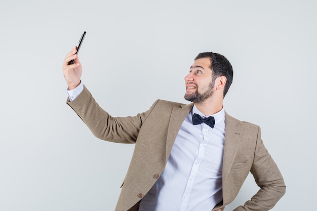 Jeune homme prenant selfie sur téléphone mobile en costume et à la joyeuse vue de face.