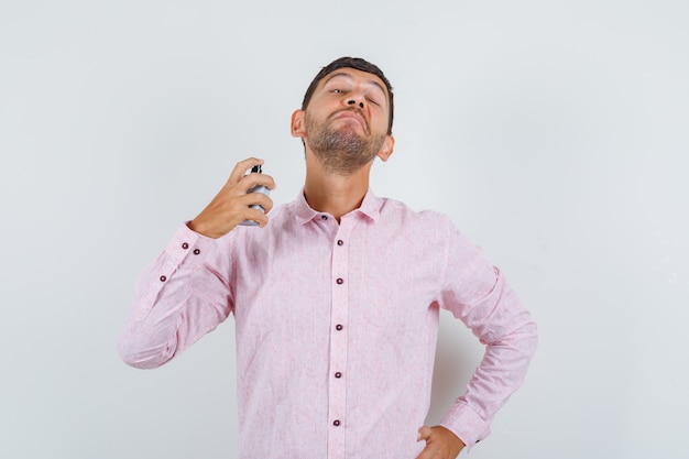 Jeune homme de pulvérisation de parfum en vue de face de chemise rose.