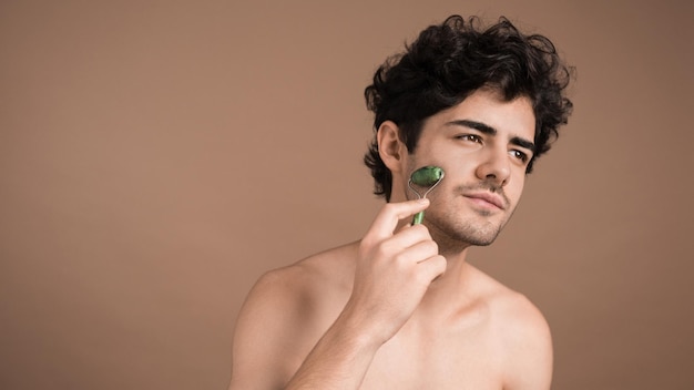 Photo gratuite un jeune homme de race blanche avec une barbe de chaume fait un massage facial à l'aide d'un rouleau