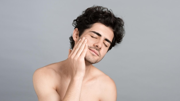 Photo gratuite un jeune homme de race blanche avec une barbe de chaume hydrate le visage et la peau avec de l'huile cosmétique