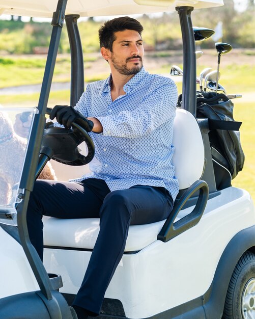 Jeune homme de race blanche dans une voiturette de golf avec son chiot Goldendoodle sur un terrain de golf professionnel