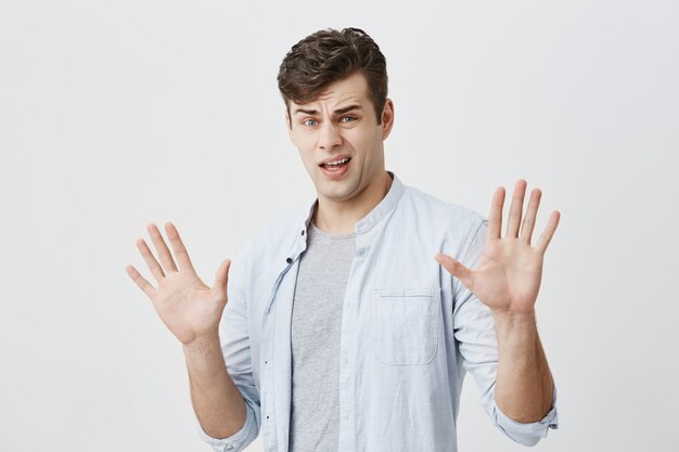 Le jeune homme de race blanche offensé a une réaction précipitée à ce qu'il a entendu, lève la main, comme dire d'arrêter cela, a une expression mécontente et en colère, isolée.