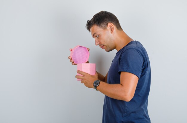 Jeune homme à la recherche dans la boîte présente ouverte en t-shirt bleu foncé et à intéressé. .