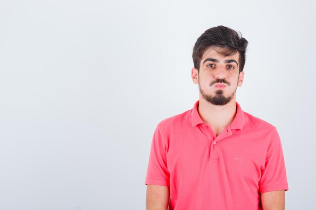 Jeune homme à la recherche d'un t-shirt rose et à l'air pensif, vue de face.