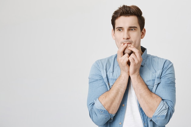 Un jeune homme réfléchi touche les lèvres et regarde ailleurs, a une idée