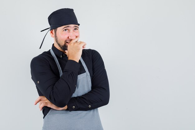 Jeune homme regardant ailleurs tout en souriant en chemise, tablier et à la pensif. vue de face.