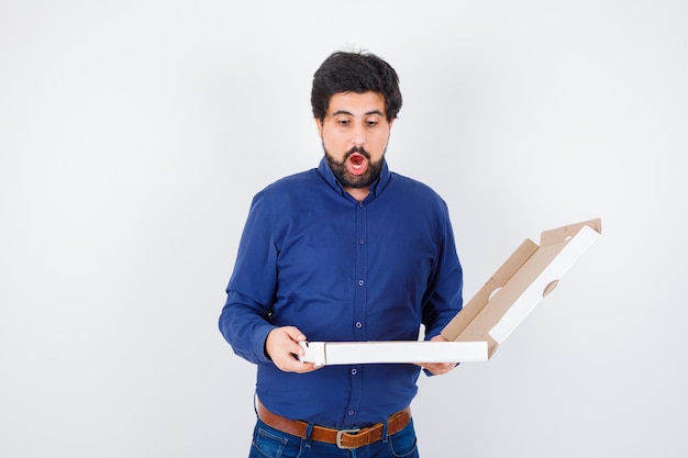 Jeune homme regardant une boîte à pizza ouverte en chemise, jeans et l'air étonné. vue de face.