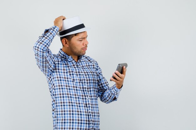 Jeune homme regardant la calculatrice en chemise à carreaux