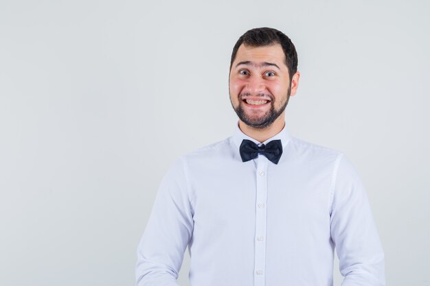 Jeune homme regardant la caméra en chemise blanche et regardant gai, vue de face.