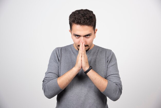 Un jeune homme regardant la caméra et mettant les mains ensemble.