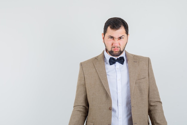 Jeune homme regardant la caméra tout en fronçant les sourcils en costume et à la vue de face, irrité.