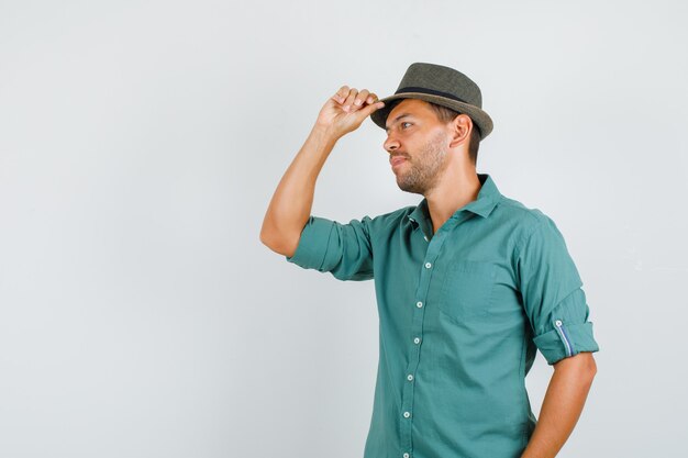 Jeune homme regardant de côté tout en tenant un chapeau en chemise et à la pensif