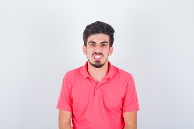 Jeune homme regardant avec les dents serrées en t-shirt rose et regardant en colère, vue de face.