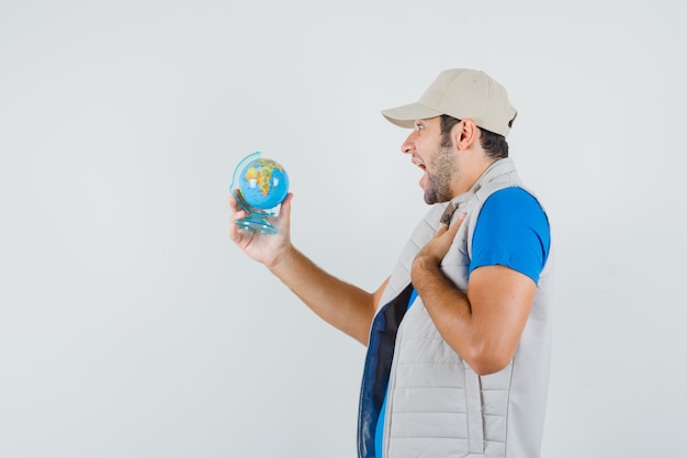 Jeune homme regardant le globe de l'école en t-shirt, veste et à la recherche de jovial.