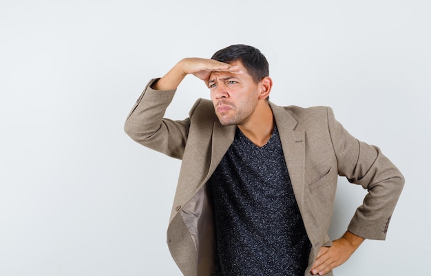 Photo gratuite jeune homme regardant loin en veste marron grisâtre, chemise noire et semblant intéressé. vue de face.