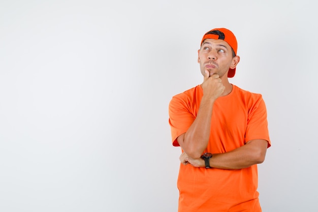 Jeune homme regardant avec la main sur le menton en t-shirt orange et casquette et à la pensif