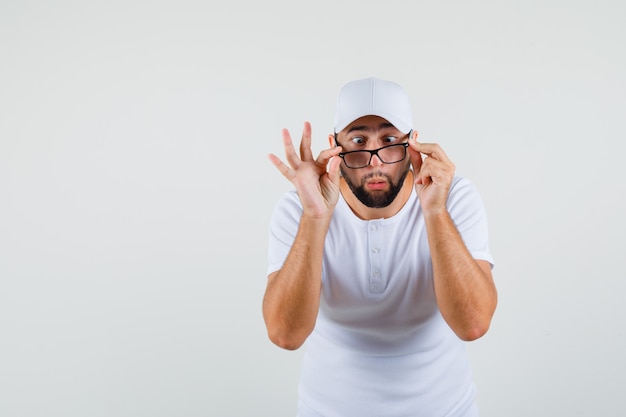 Jeune Homme Regardant Par-dessus Des Lunettes Avec Des Yeux Strabisme En T-shirt Blanc Et à La Drôle, Vue De Face.