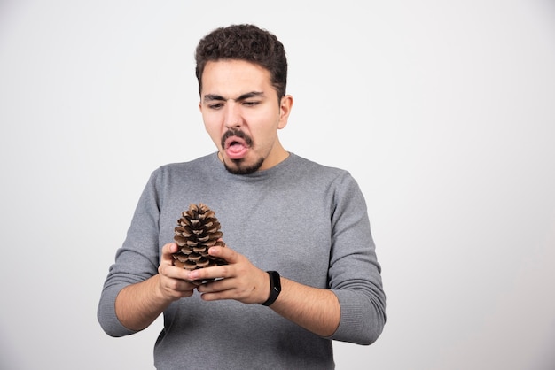 Un jeune homme regardant une pomme de pin avec dégoût.