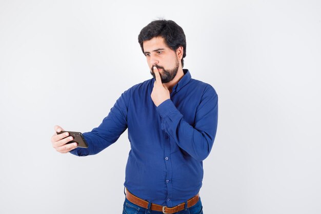 Jeune Homme Regardant Le Téléphone En Pensant En Vue De Face De La Chemise Bleu Royal.