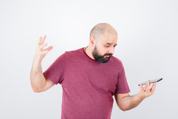 Jeune homme regardant le téléphone en t-shirt rose et l'air ennuyé, vue de face.