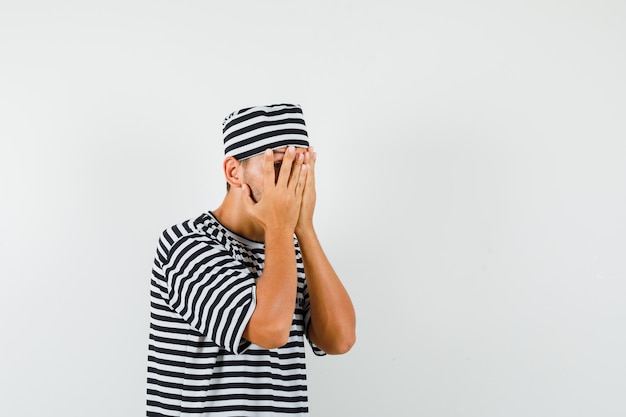 Jeune homme regardant à travers les doigts en chapeau t-shirt rayé et à la peur