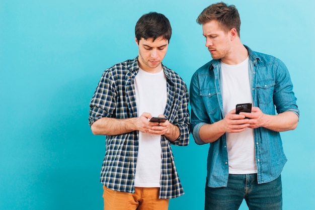 Jeune homme regarde son ami textos sur smartphone sur fond bleu