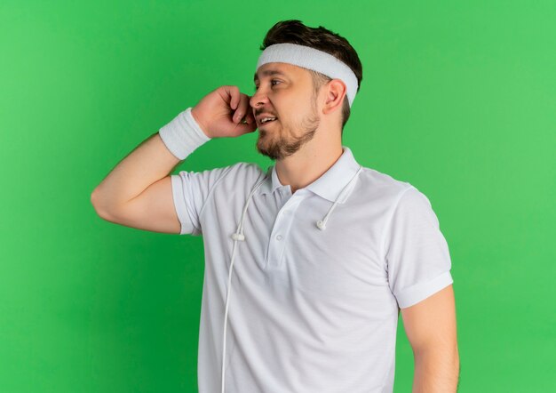 Jeune homme de remise en forme en chemise blanche avec bandeau à côté avec sourire sur le visage debout sur fond vert