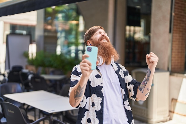 Jeune homme rousse utilisant un smartphone avec une expression gagnante dans la rue