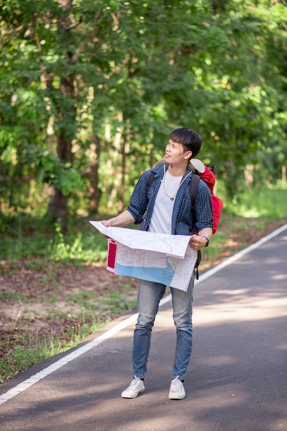 Jeune homme routard voyageur avec carte, il porte un grand sac à dos pendant la détente en plein air pendant les vacances d'été en forêt, espace de copie