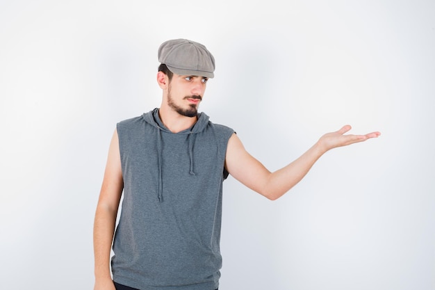 Jeune homme s'étendant d'une main comme tenant quelque chose en t-shirt gris et casquette et à la sérieuse