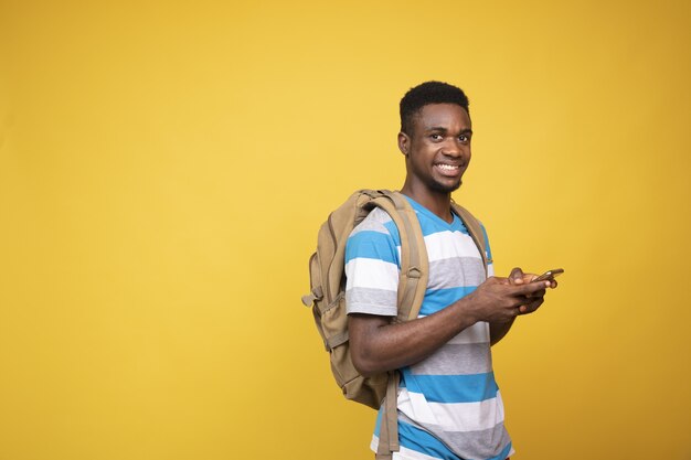 Jeune homme avec un sac à dos à l'aide de son téléphone sur fond jaune
