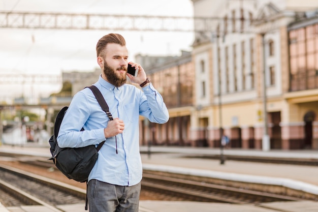 Photo gratuite jeune homme avec sac à dos, parler au téléphone portable à la gare