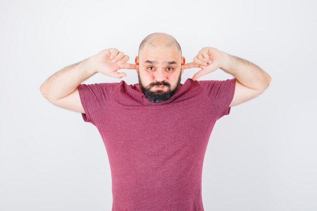 Jeune homme se branchant les oreilles avec les doigts tout en gonflant ses joues en vue de face d'un t-shirt rose.