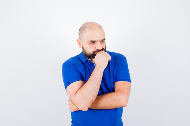 Jeune homme se concentrant sur quelque chose en chemise bleue et regardant pensif, vue de face.